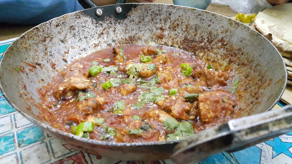 Chicken karahi in a metal pan garnished with coriander and green chillies